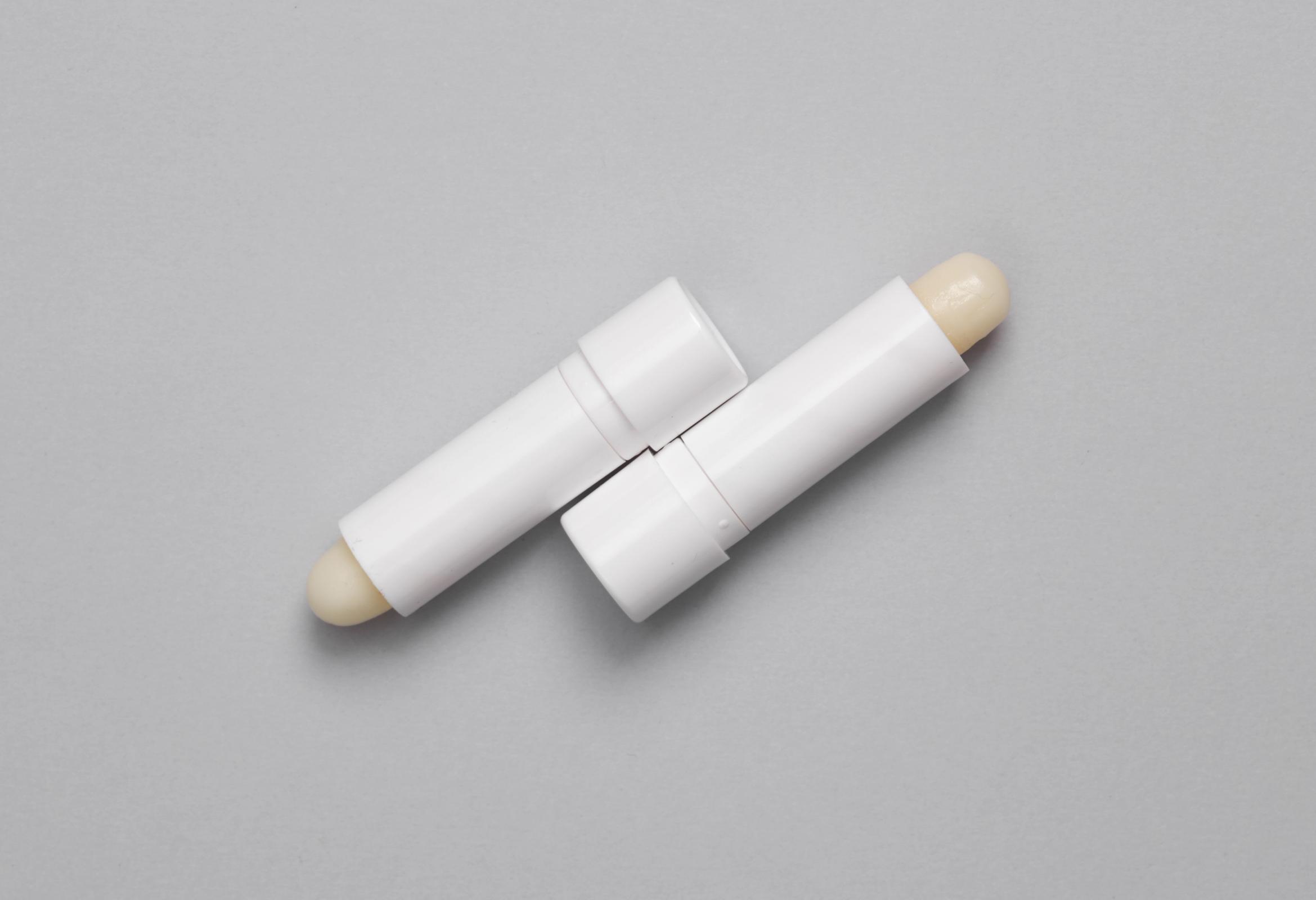 dos tubos blancos de bálsamo labial sobre un fondo gris.