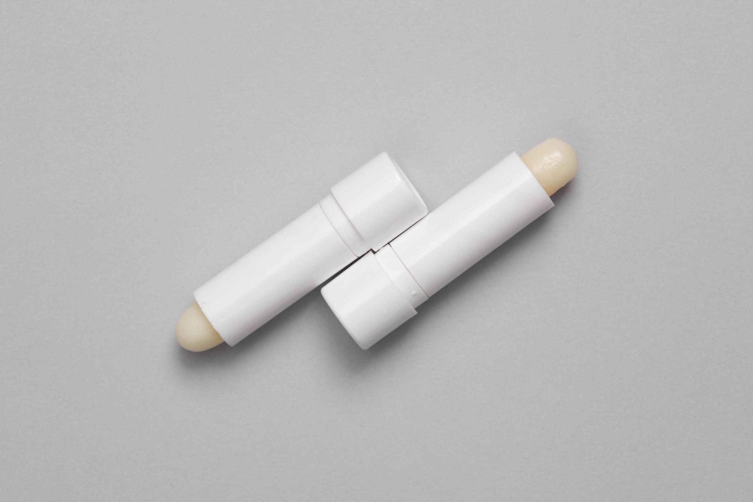 dos tubos blancos de bálsamo labial sobre un fondo gris.