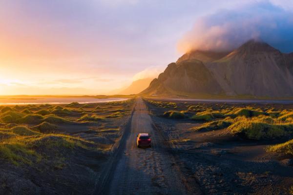 an aerial view of a car driving down a dirt road at sunset .