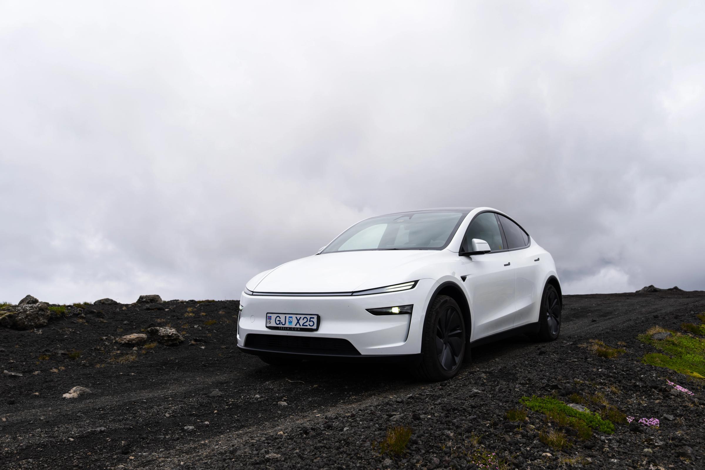 Tesla Model Y estacionado sobre grava volcánica negra bajo el cielo nublado de Islandia, vehículo de conducción autónoma