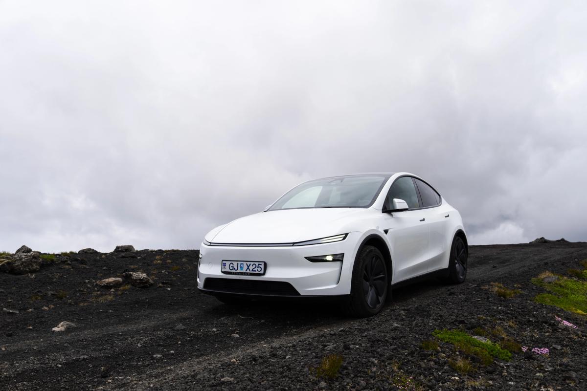 Tesla Model Y estacionado sobre grava volcánica negra bajo el cielo nublado de Islandia, vehículo de conducción autónoma