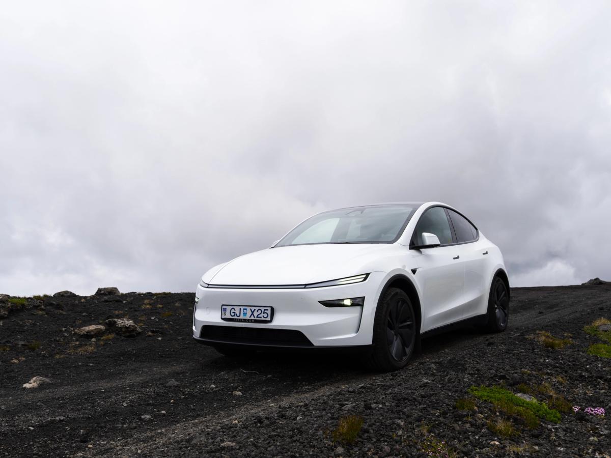 Sobre terreno de lava negra Tesla Model Y estacionado sobre grava volcánica negra bajo el cielo nublado de Islandia, vehículo de conducción autónoma