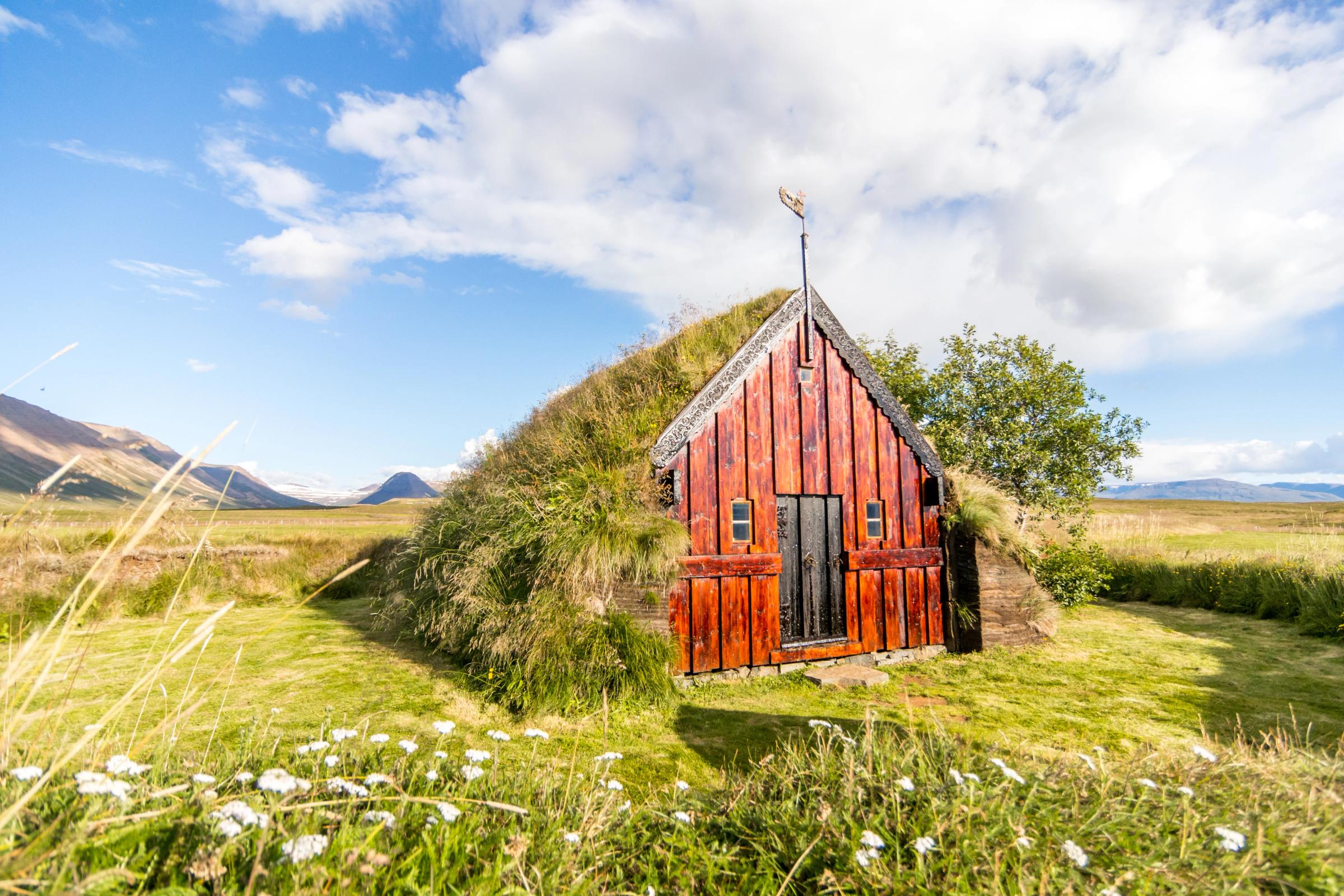 a small red house is sitting in the middle of a grassy field .