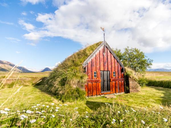a small red house is sitting in the middle of a grassy field .