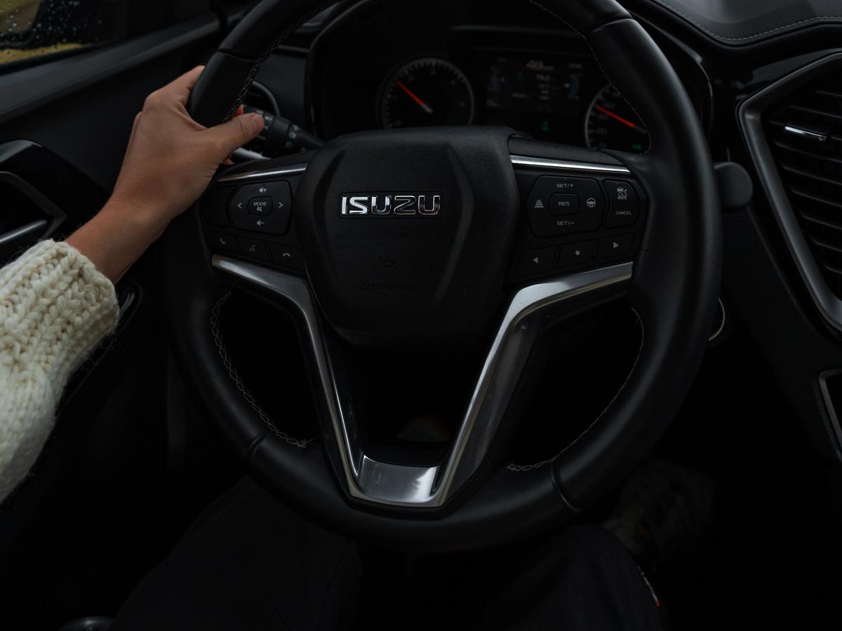 Funda para volante Mano con una manga de punto sobre el volante y un camino de grava visible al frente