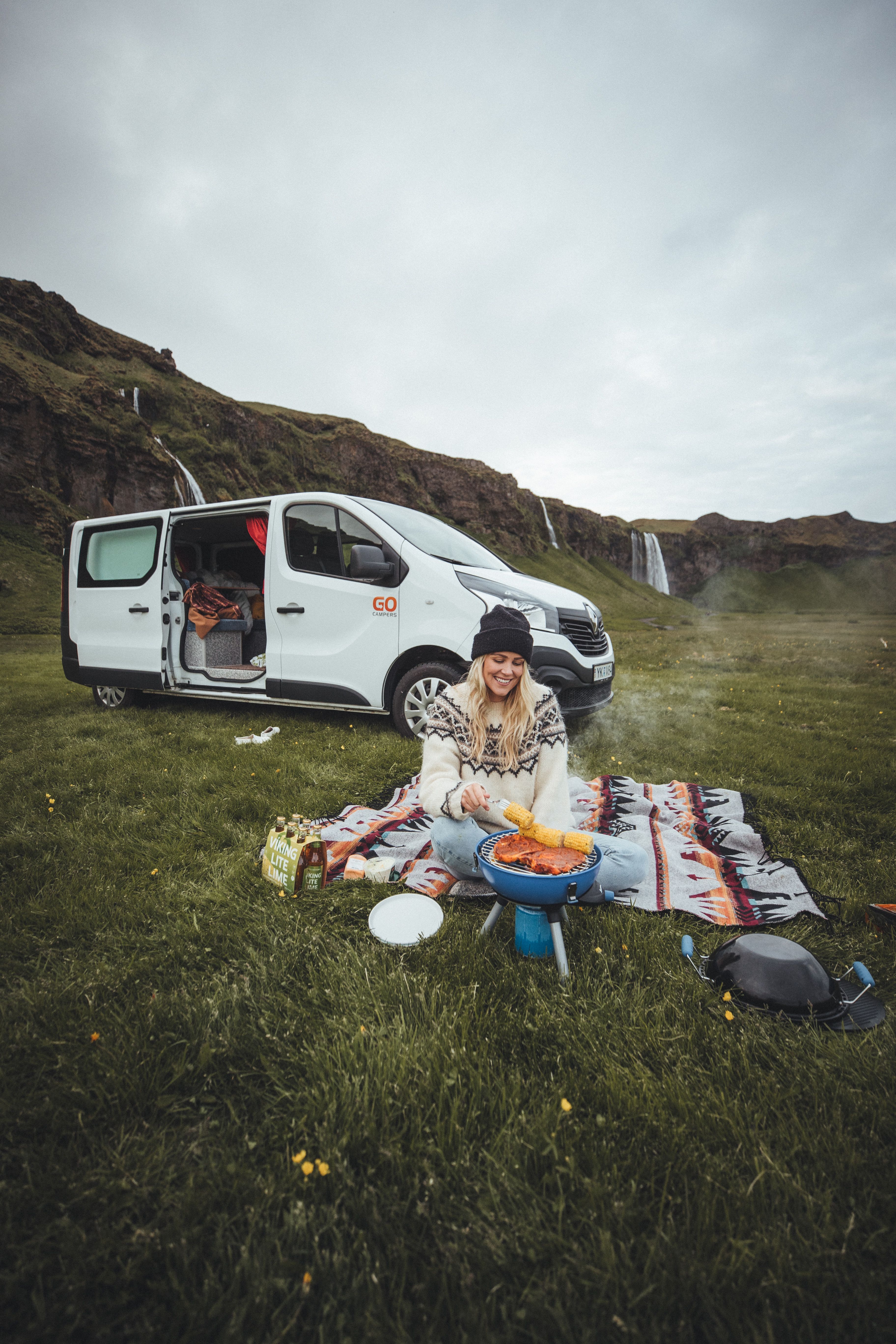a woman is sitting on a blanket cooking food in front of a van .
