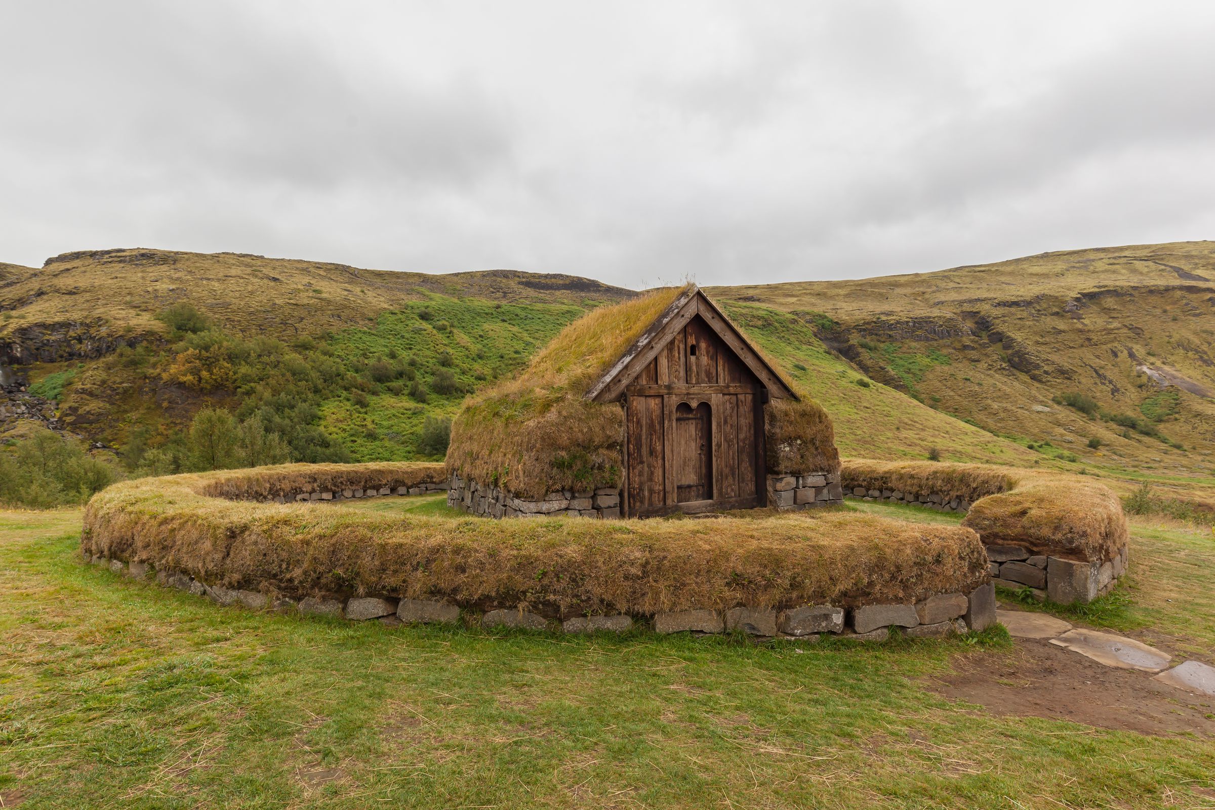 a small wooden house surrounded by grass and rocks in the middle of a field .
