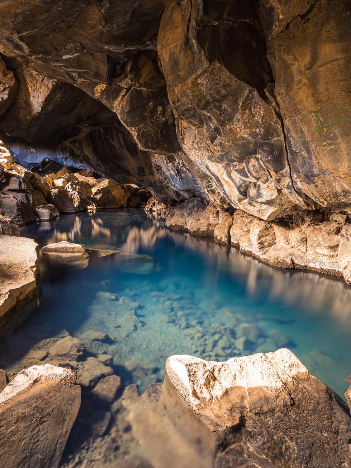 A natural cave with a clear blue pool of water surrounded by rocky walls.