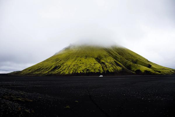 a car is driving down a dirt road in front of a green mountain covered in fog .