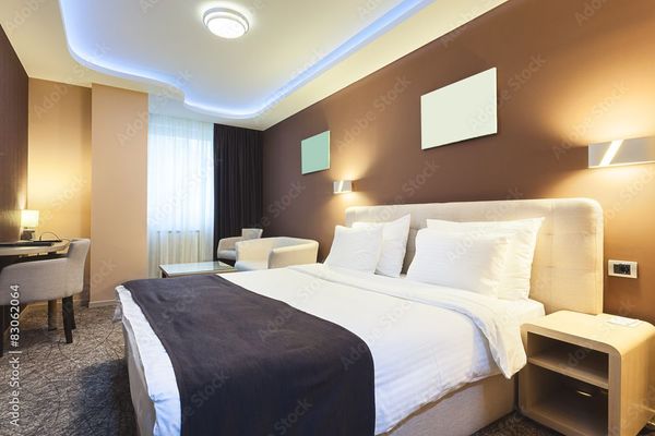 A modern hotel room with a large bed, brown accent wall, desk, and blue ceiling lights.