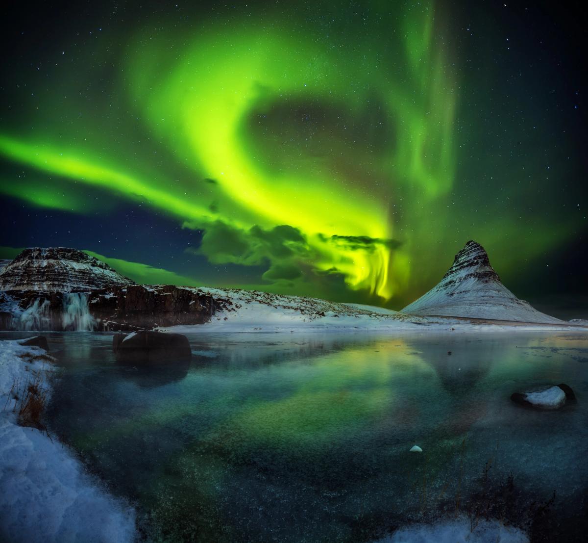 la aurora boreal se refleja en el agua de un lago.