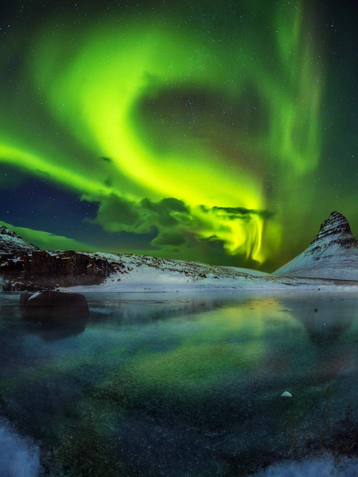 la aurora boreal se refleja en el agua de un lago.