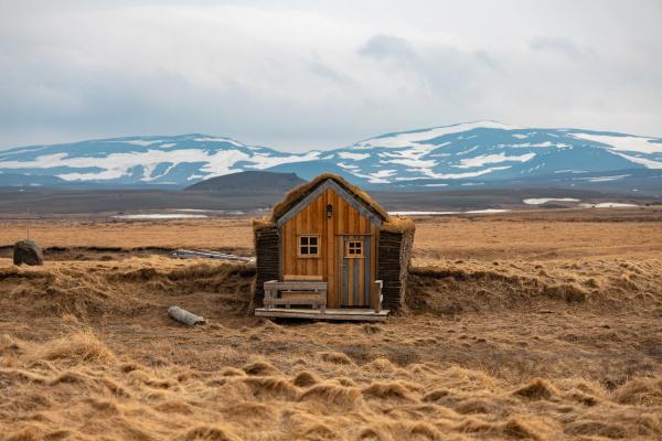 una pequeña casa de madera en medio de un campo con montañas en el fondo .