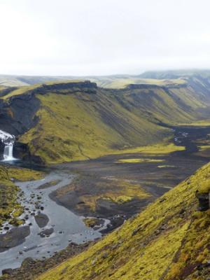 A deep, moss-covered valley with a multi-tiered waterfall flowing into a dark, winding river.