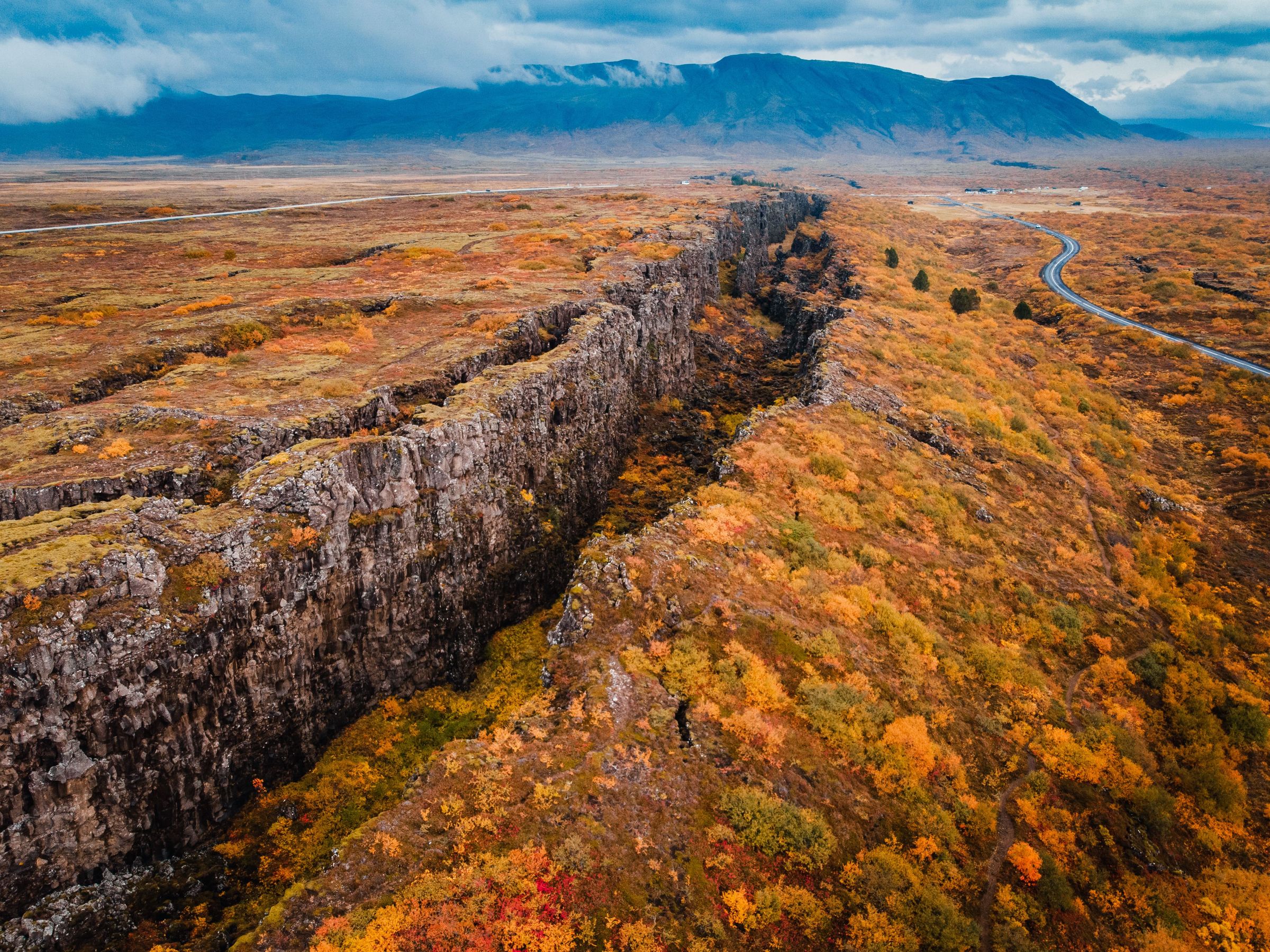 una vista aérea de una persona de pie en la cima de una montaña rodeada de hojas de otoño.