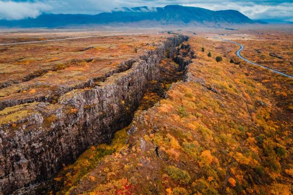 una vista aérea de una persona de pie en la cima de una montaña rodeada de hojas de otoño.