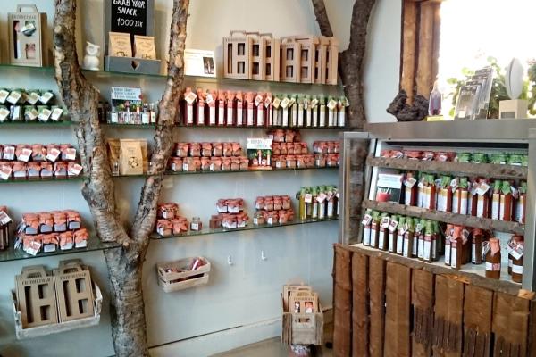 Interior of a rustic store with glass shelves built around a tree trunk, displaying many jars and bottles of food products.