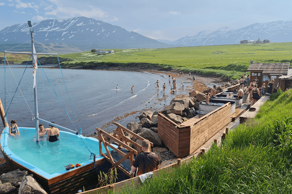 a group of people are swimming in a pool near a body of water at tröllaskagi in iceland.