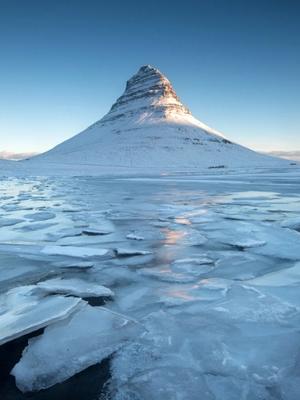 a mountain covered in snow and ice is surrounded by a frozen lake at Kirkjufell in Iceland.