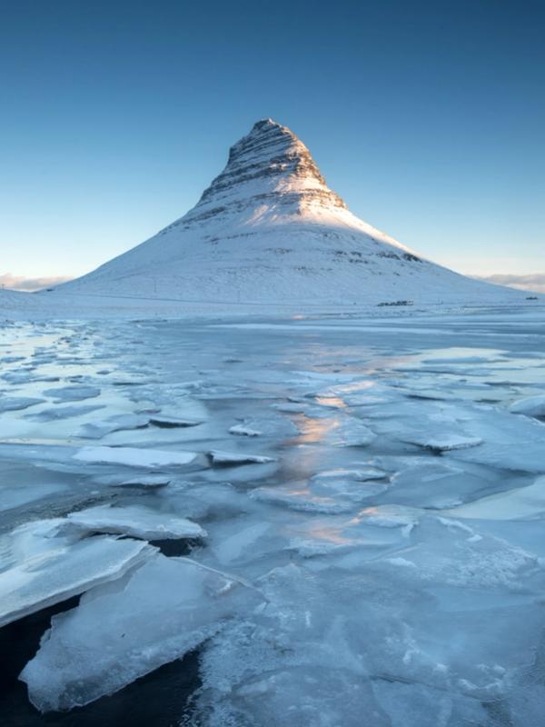 a mountain covered in snow and ice is surrounded by a frozen lake at Kirkjufell in Iceland.