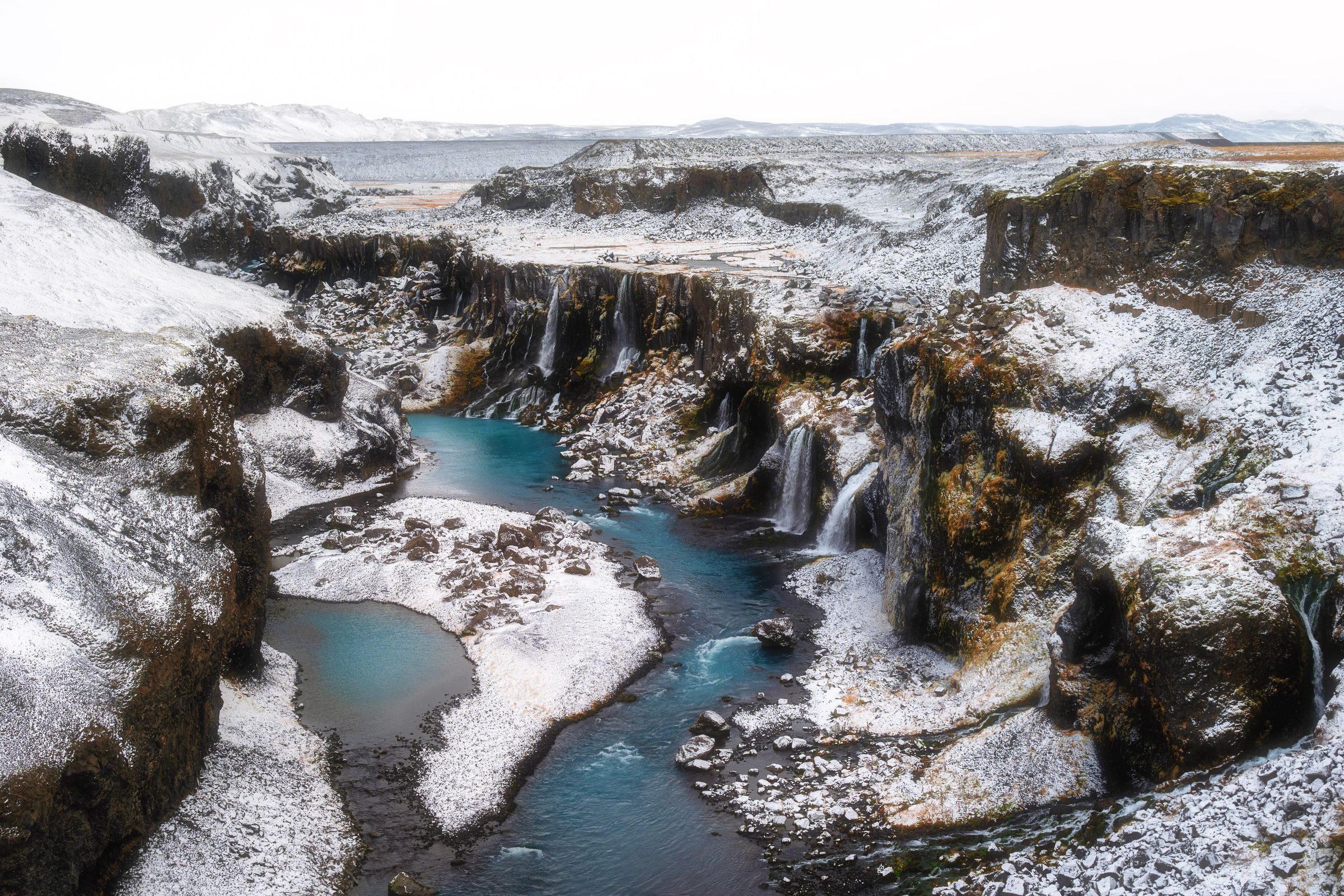 Un río de un azul vibrante fluye a través de un cañón cubierto de nieve con cascadas.