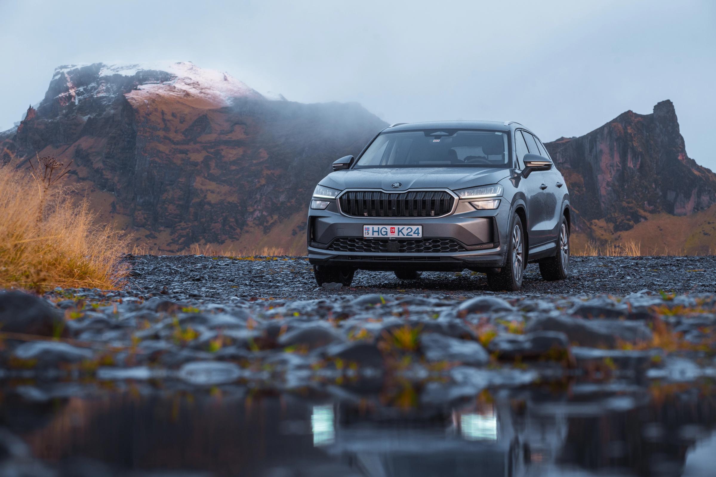 SUV Skoda Kodiaq de aluguer na Islândia, estacionado numa estrada de gravilha molhada, com montanhas ao fundo