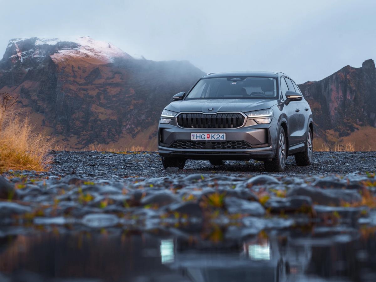 Vista frontal do Skoda Kodiaq na montanha SUV Skoda Kodiaq de aluguer na Islândia, estacionado numa estrada de gravilha molhada, com montanhas ao fundo