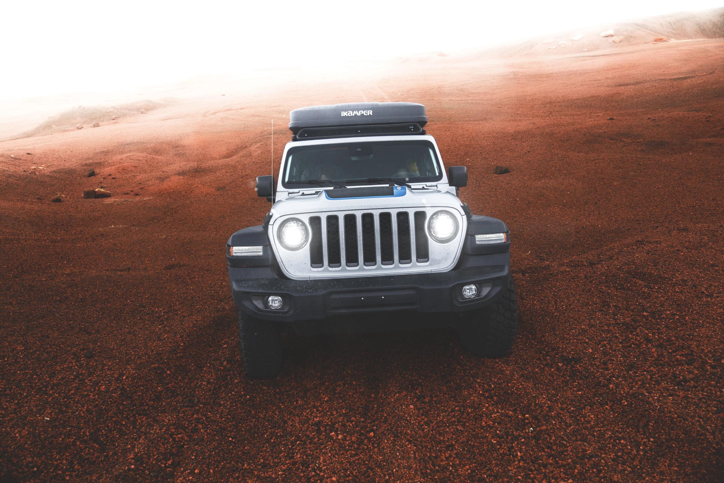 Front view of the camper with headlights on across red gravel terrain, 4x4 campervan rental Iceland