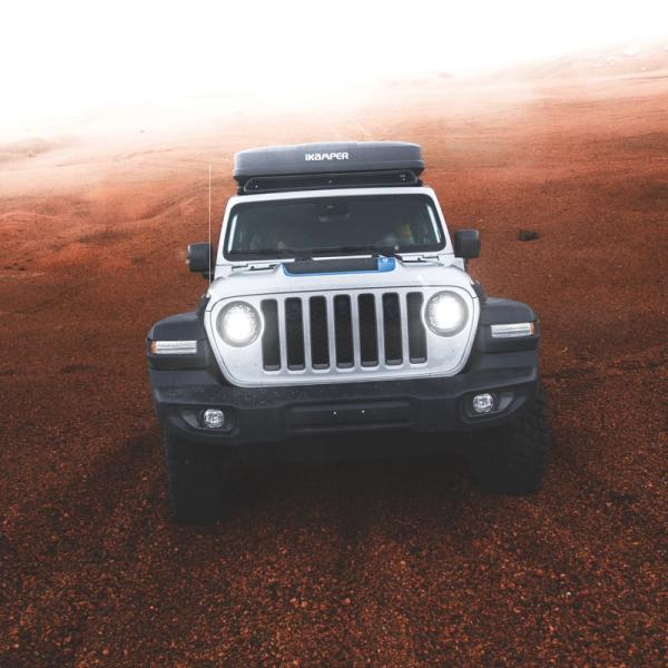 White Jeep with rooftop tent on red rocky terrain.