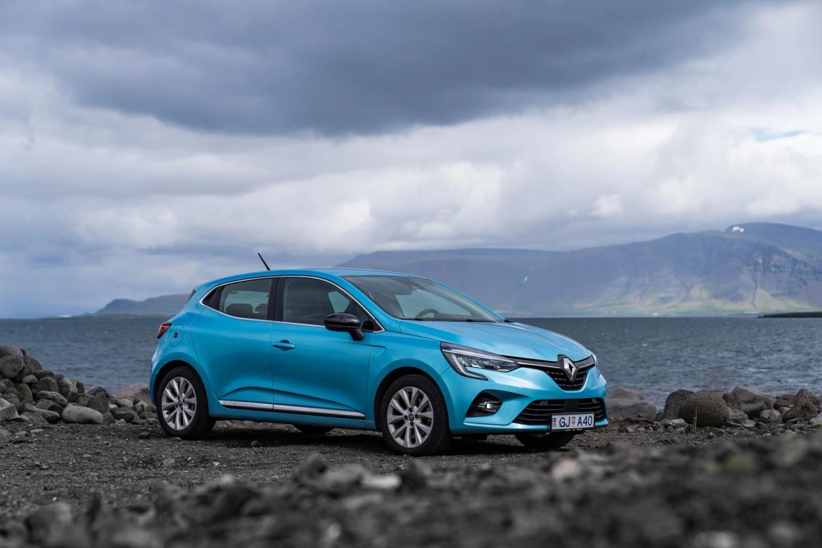 Kompaktwagen Renault Clio schräg von vorn, geparkt an einem felsigen Ufer mit Bergen im Hintergrund