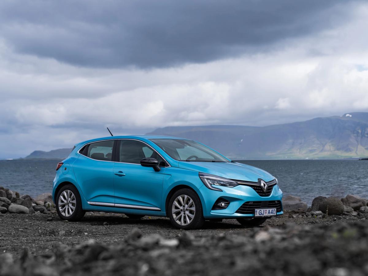 Clio – Vorderansicht schräg vor Küstenkulisse Kompaktwagen Renault Clio schräg von vorn, geparkt an einem felsigen Ufer mit Bergen im Hintergrund