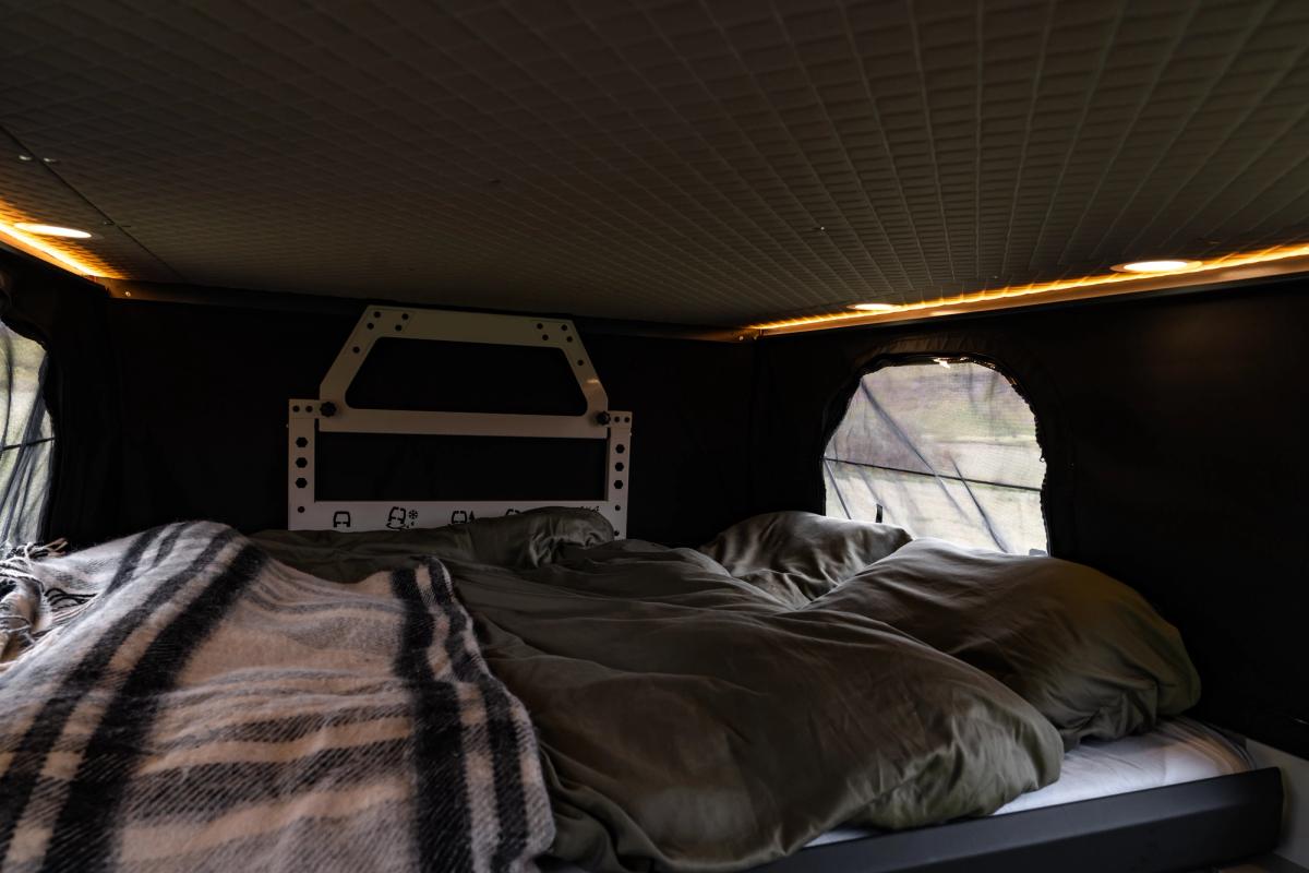 Cama preparada en el techo elevable, con una manta de cuadros, almohadas y una ventana lateral