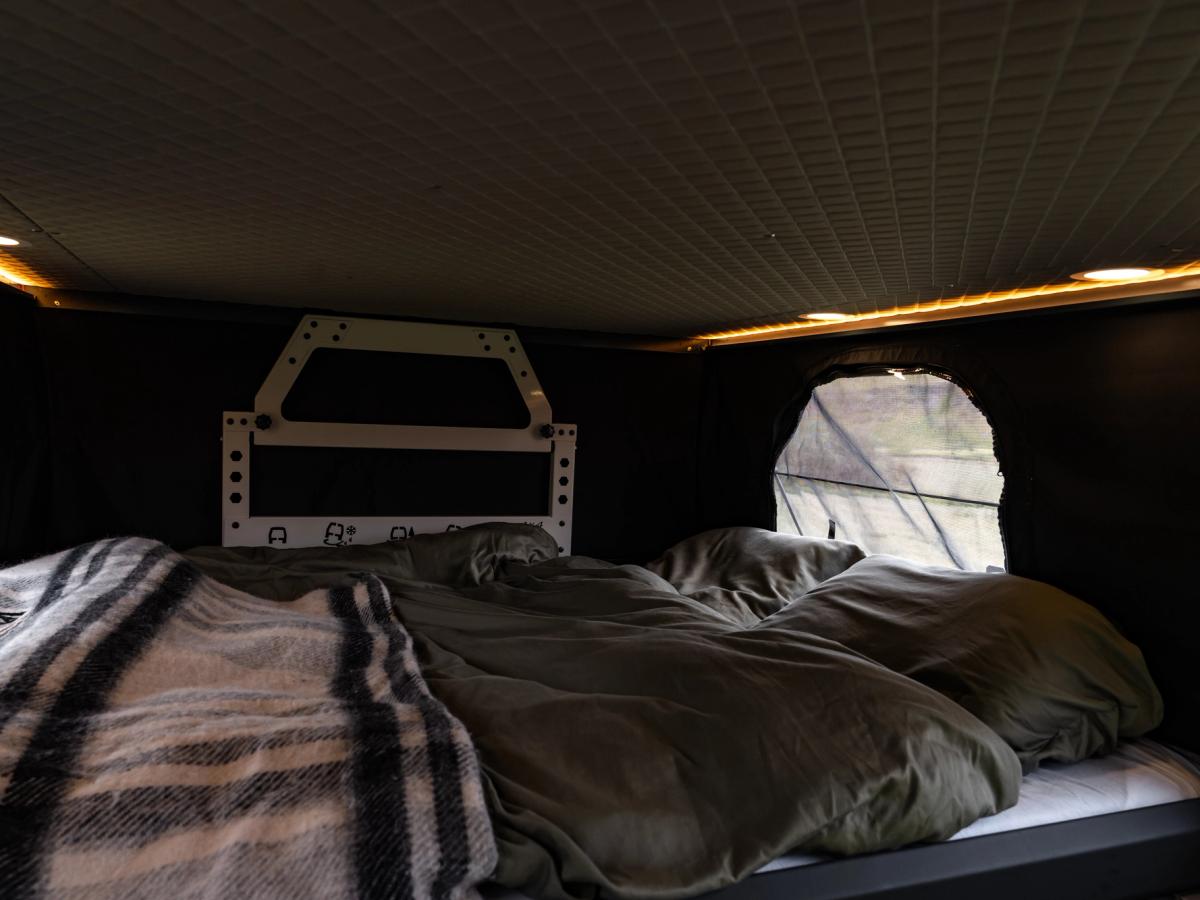 Cama en techo elevable Cama preparada en el techo elevable, con una manta de cuadros, almohadas y una ventana lateral
