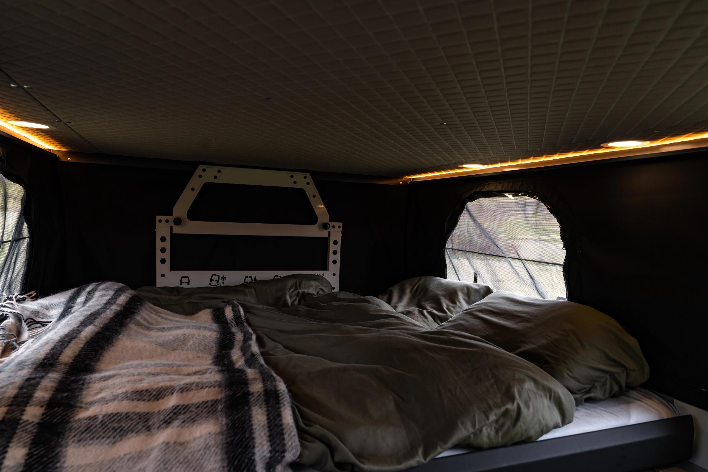 Cama en techo elevable Cama preparada en el techo elevable, con una manta de cuadros, almohadas y una ventana lateral
