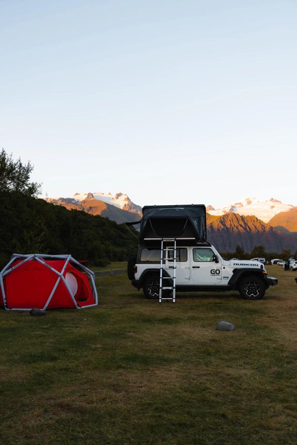 A 4x4 campervan with ladder down at a grassy campsite next to a red ground tent