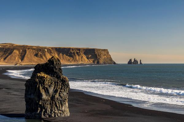 a large rock sitting on top of a black sandy beach next to the ocean .