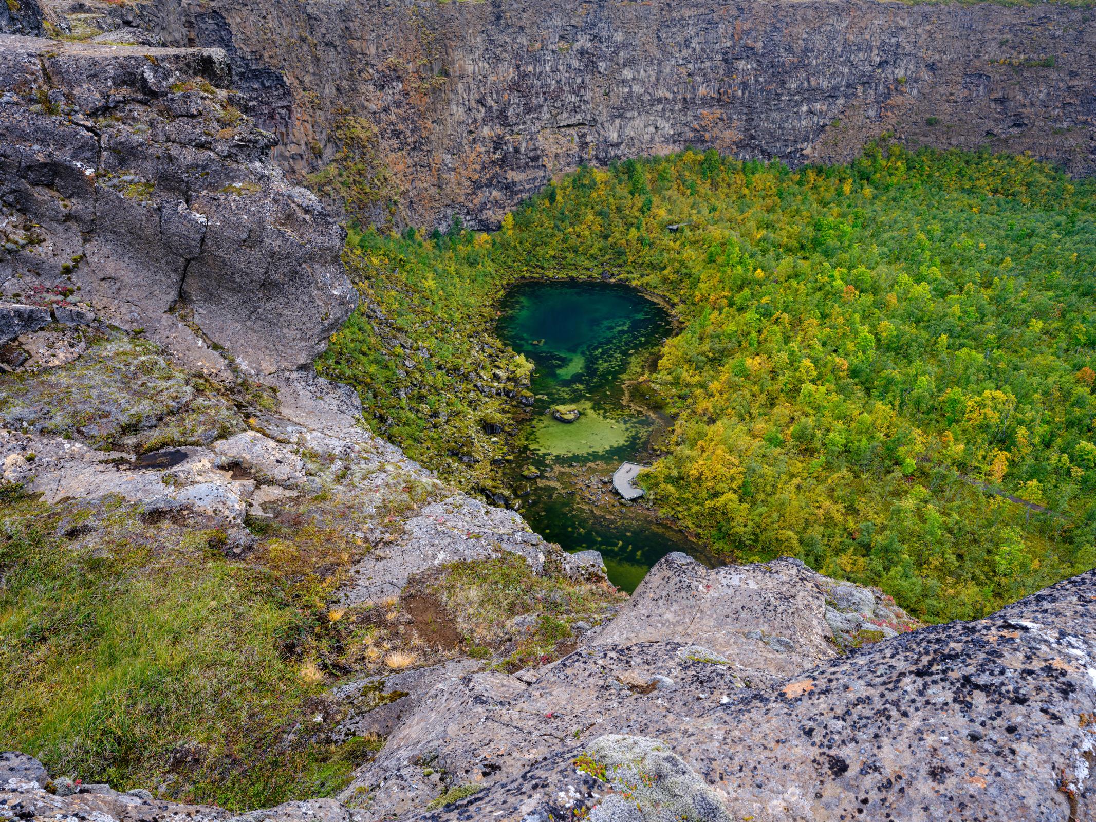 Pond in the middle of a green forest surrounded by cliffs