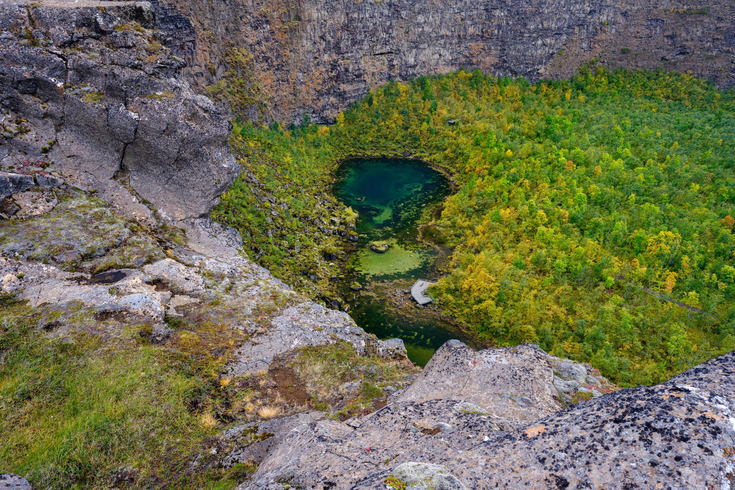 Pond in the middle of a green forest surrounded by cliffs