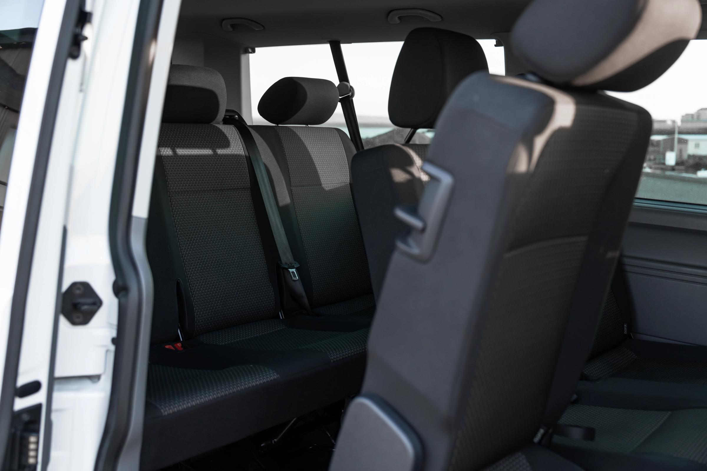 Rücksitzbank und umklappbare mittlere Sitzreihe eines Volkswagen Caravelle, durch die offene Tür gesehen