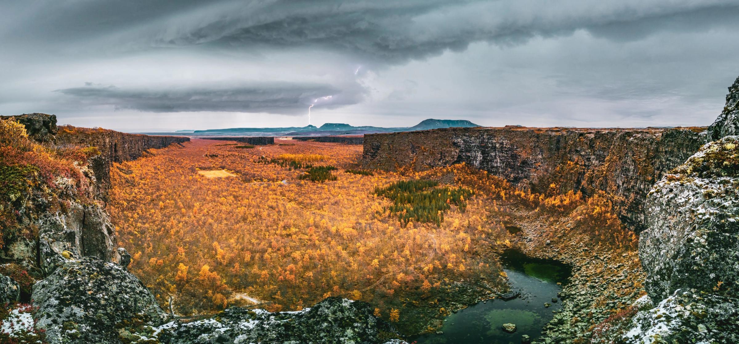 Walls surrounding Asbyrgi canyon with orange trees on autumn with lightning