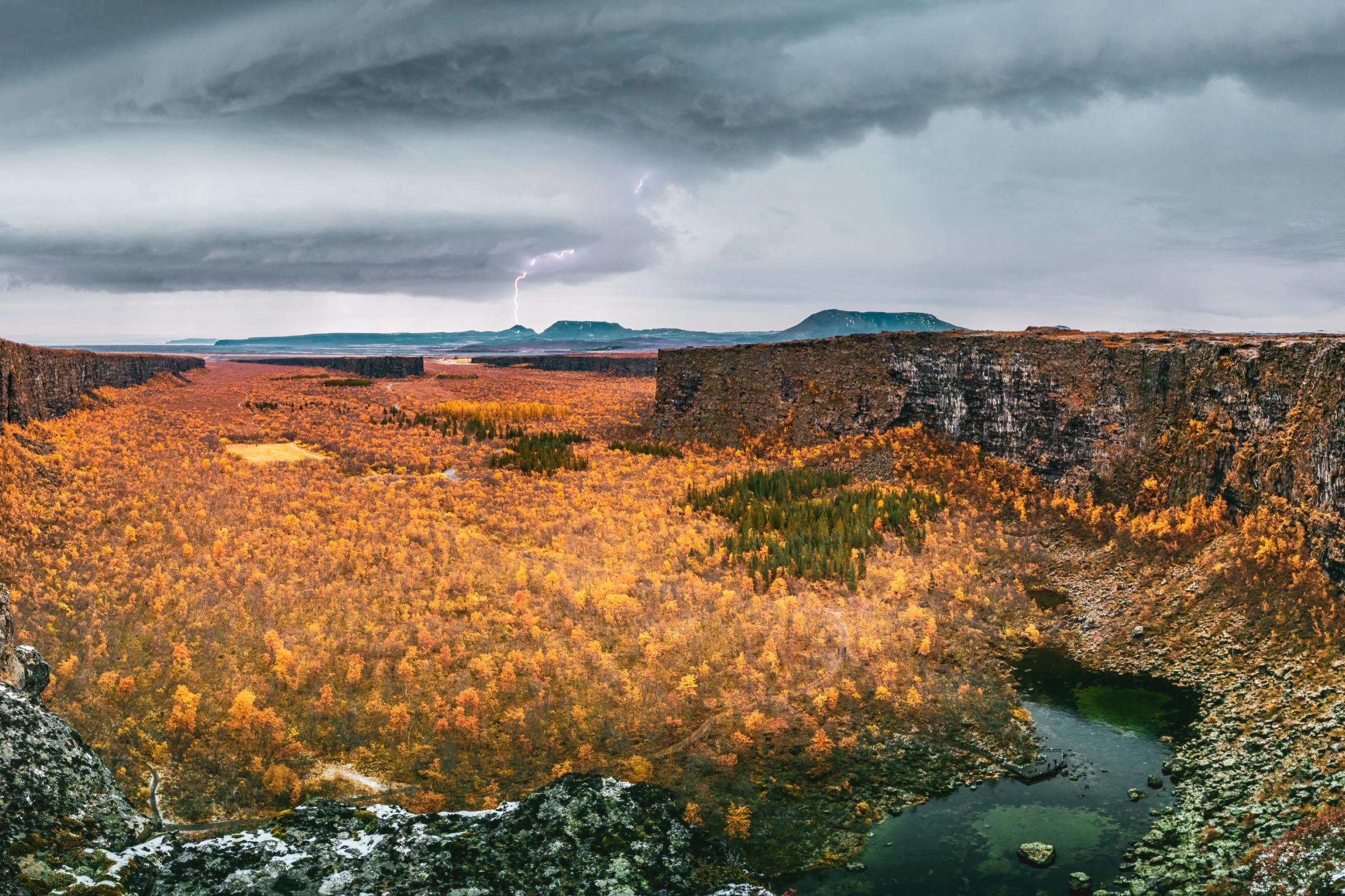 Walls surrounding Asbyrgi canyon with orange trees on autumn with lightning
