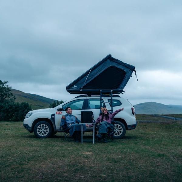 un homme et une femme sont assis devant une voiture avec une tente au-dessus de celle-ci.