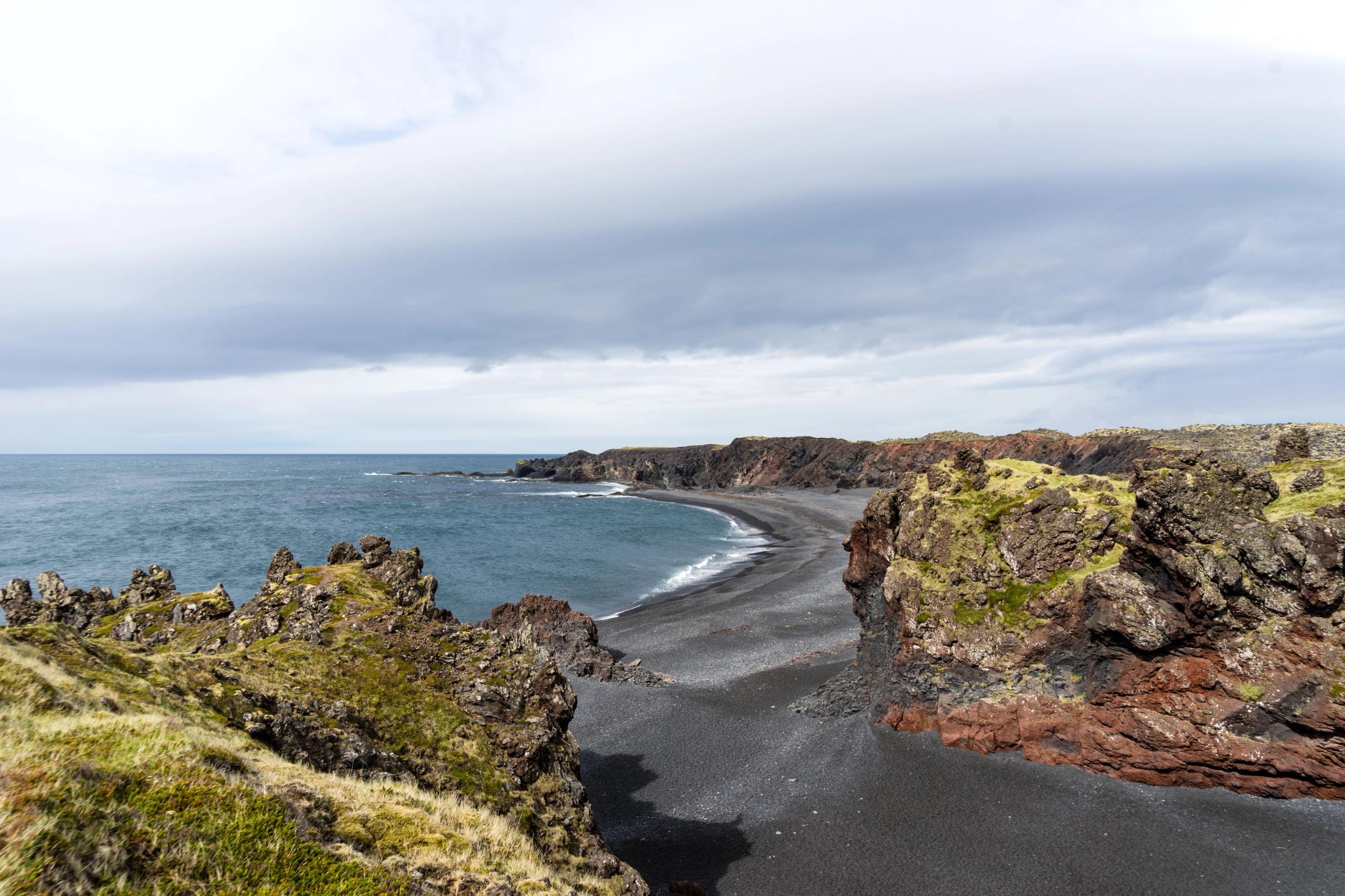 there is a black sandy beach in the middle of the ocean .