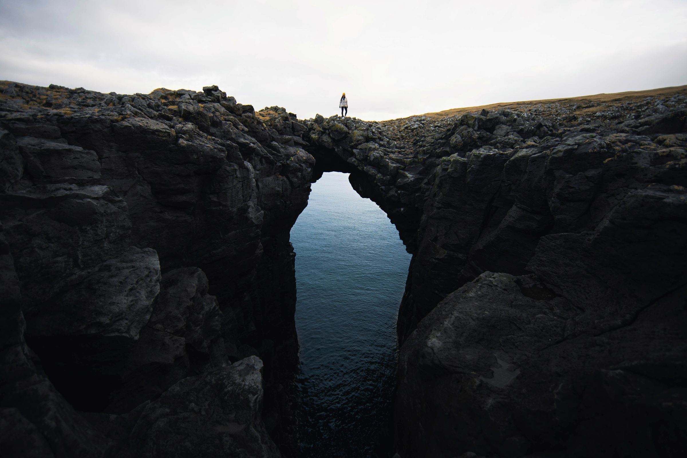 a person is standing on top of a rocky cliff overlooking the ocean .