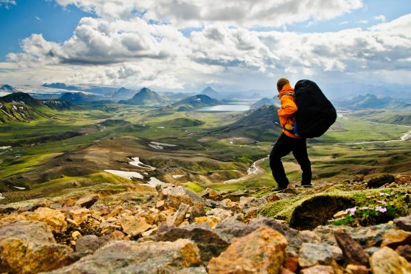 a man with a backpack is standing on top of a mountain .