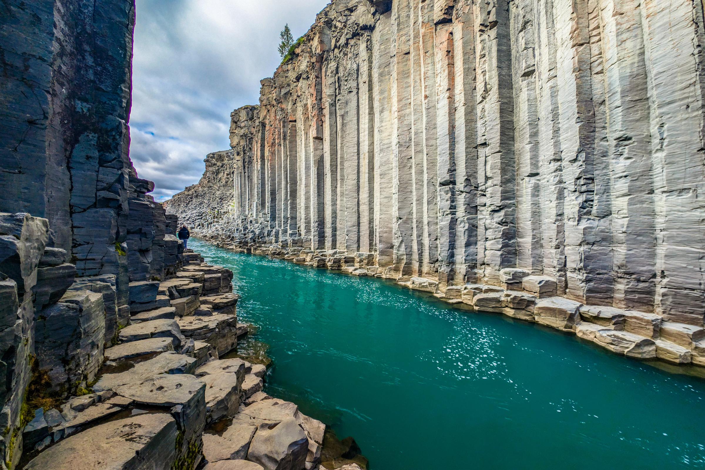 A canyon with a turquoise river flowing between towering hexagonal basalt columns.