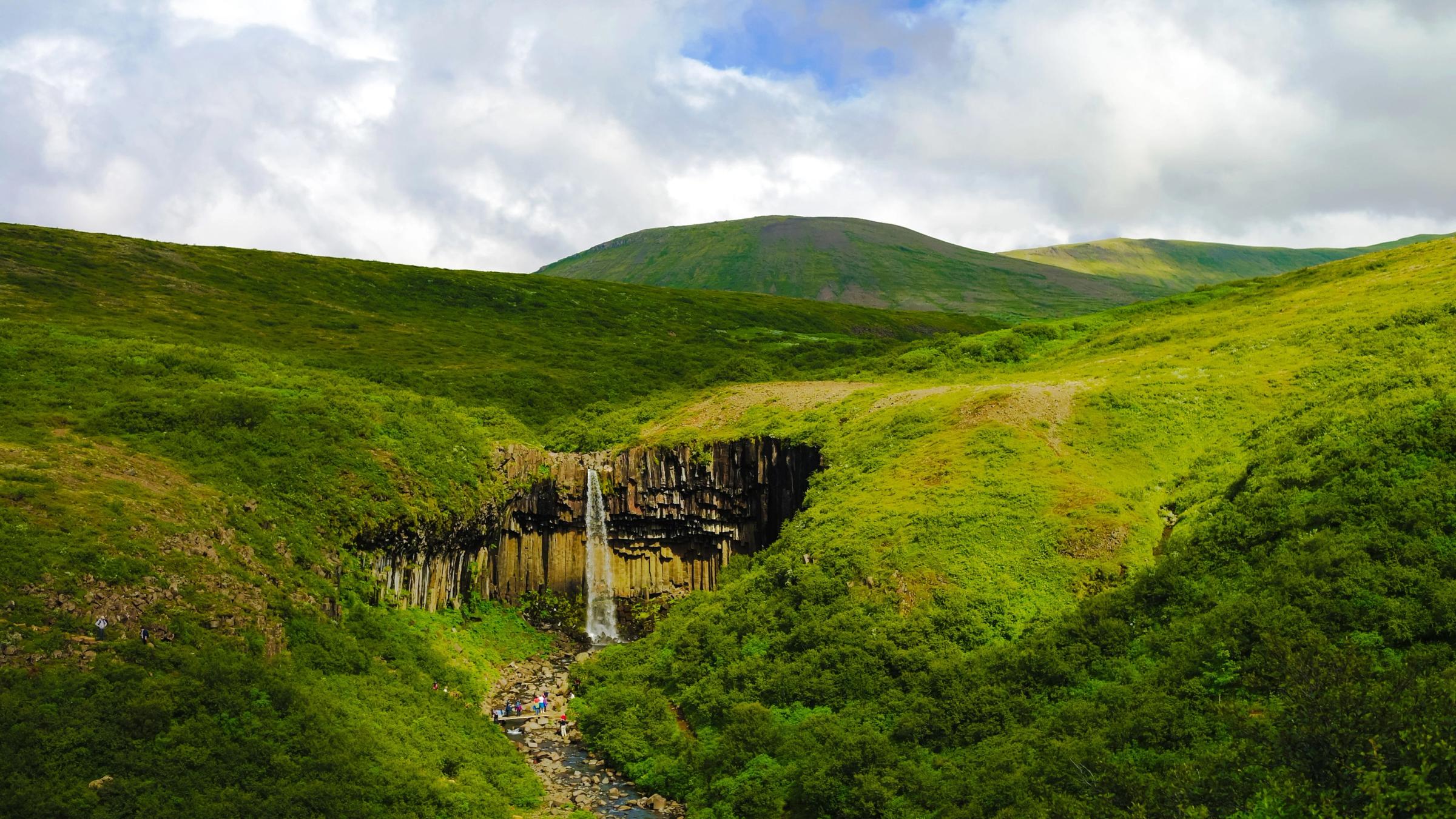 una cascada en medio de un valle verde y exuberante rodeado de montañas.