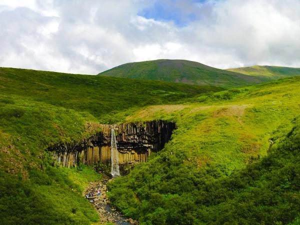 una cascada en medio de un valle verde y exuberante rodeado de montañas.