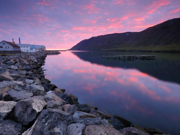 cuerpo de agua con casas en una orilla y montes en la otra al atardecer