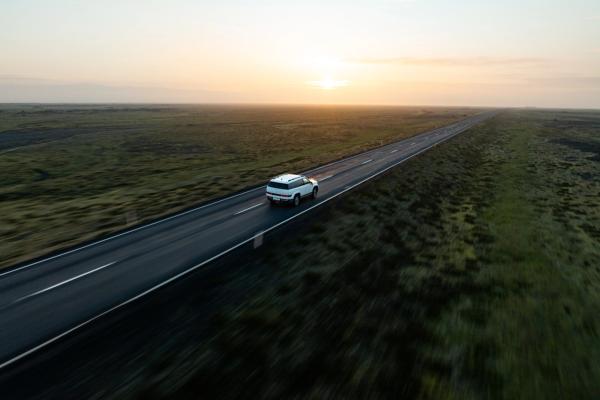 White SUV driving on a straight road through a vast, green landscape at sunset.